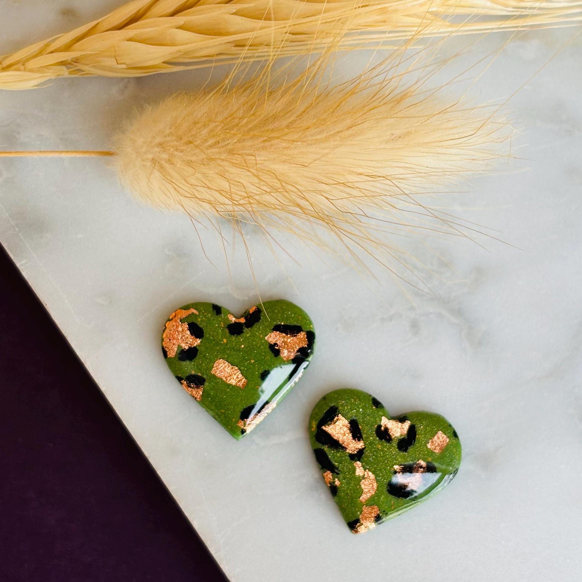Elegant heart-shaped stud earrings with a hand-painted leopard print, handmade with polymer clay.
