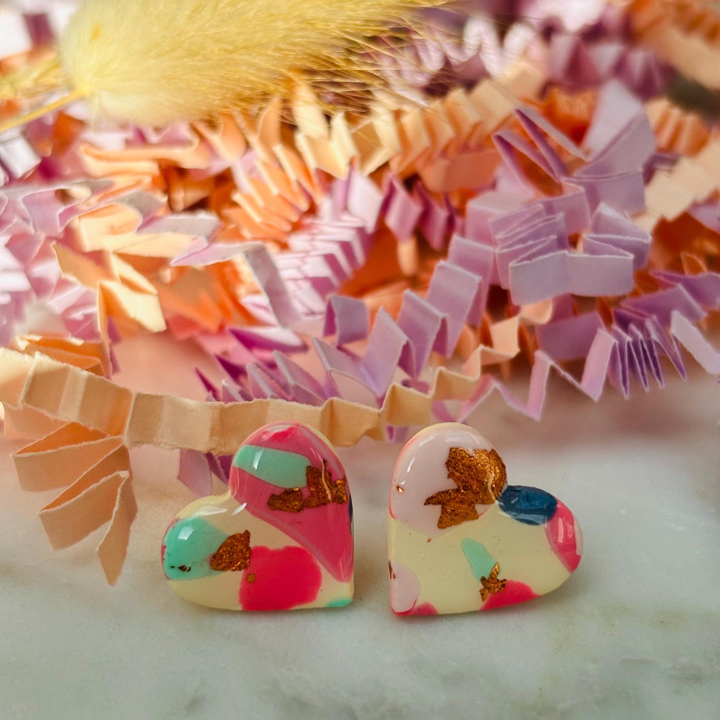 Soft pink heart-shaped stud earrings with rose gold accents, handmade with polymer clay.