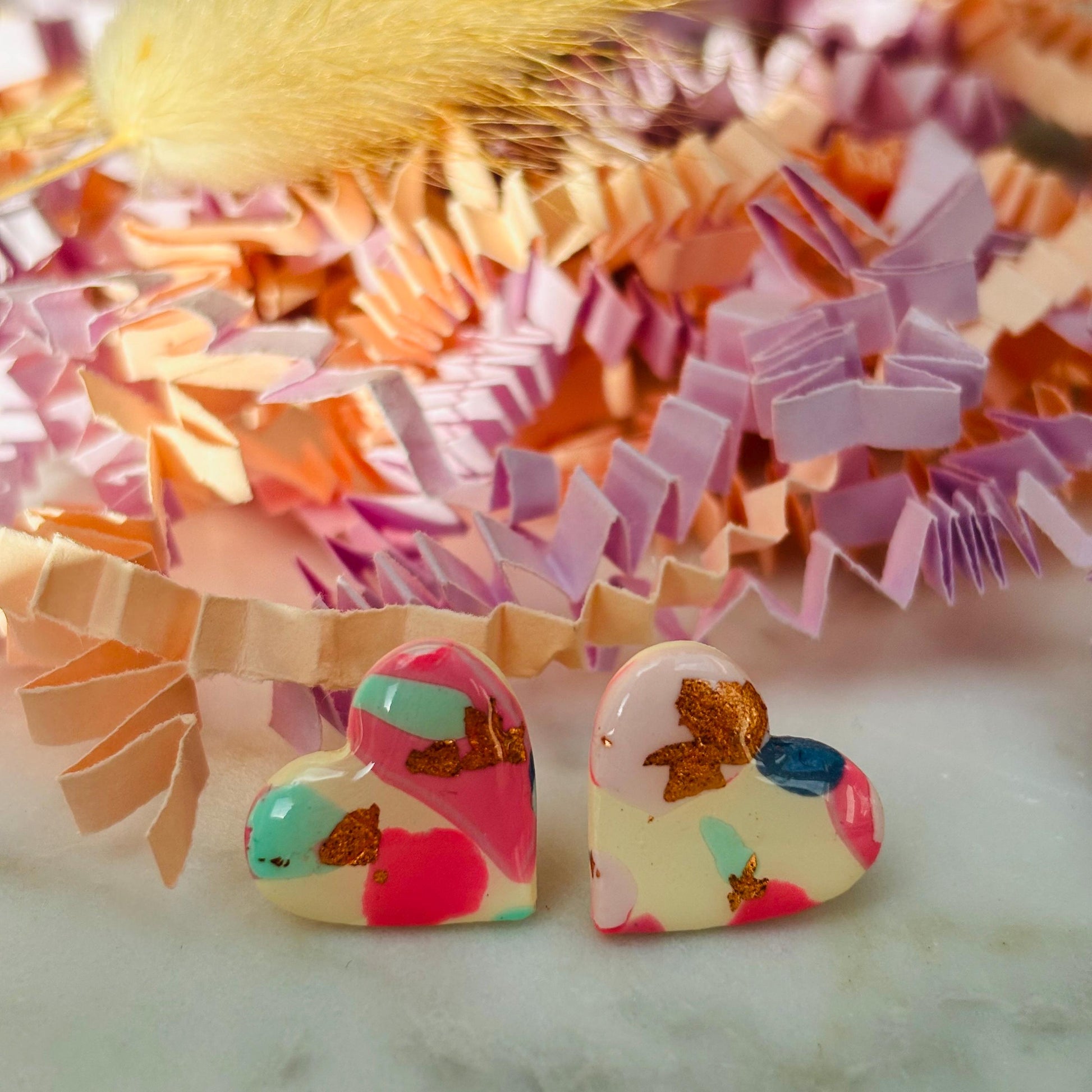 Soft pink heart-shaped stud earrings with rose gold accents, handmade with polymer clay.
