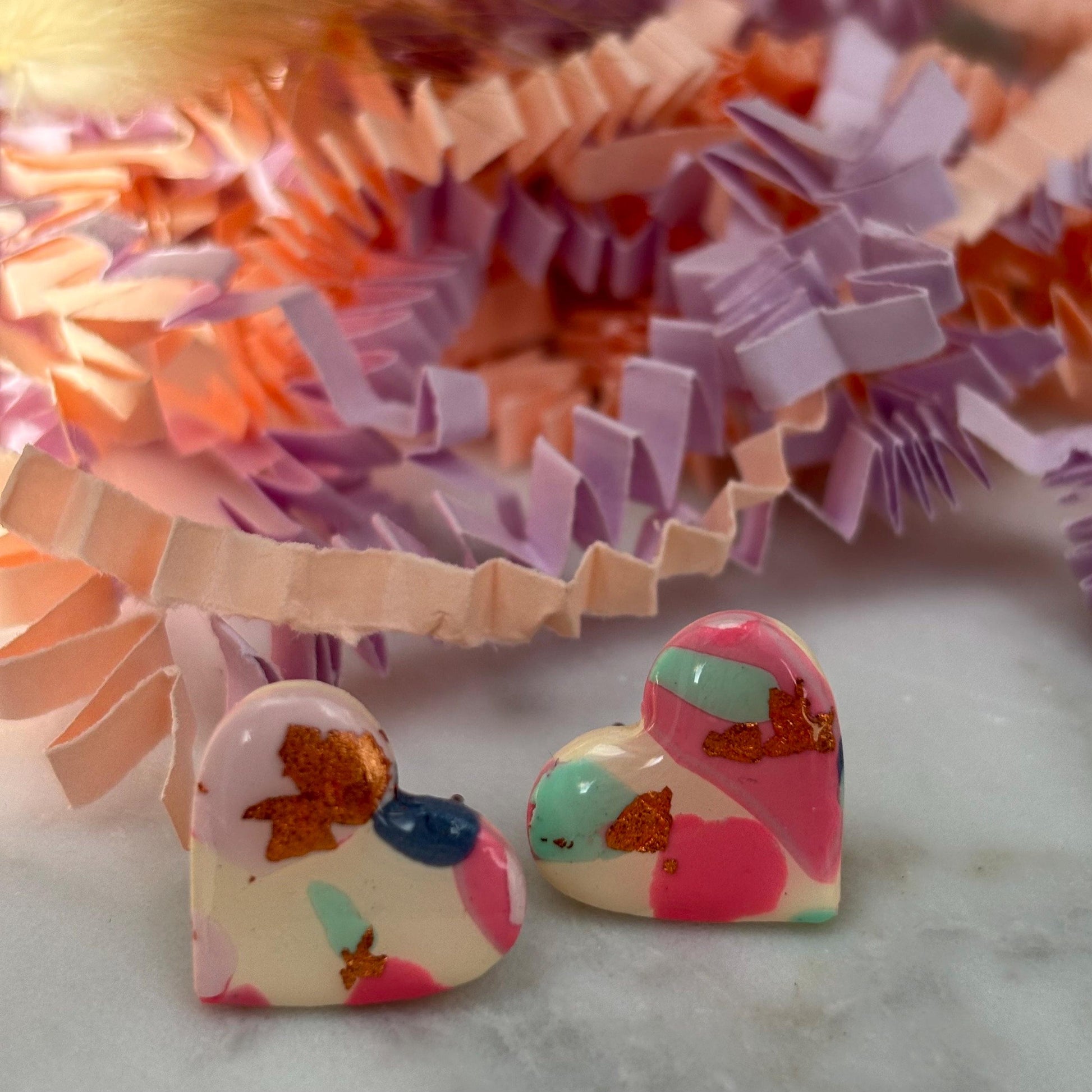 Soft pink heart-shaped stud earrings with rose gold accents, handmade with polymer clay.