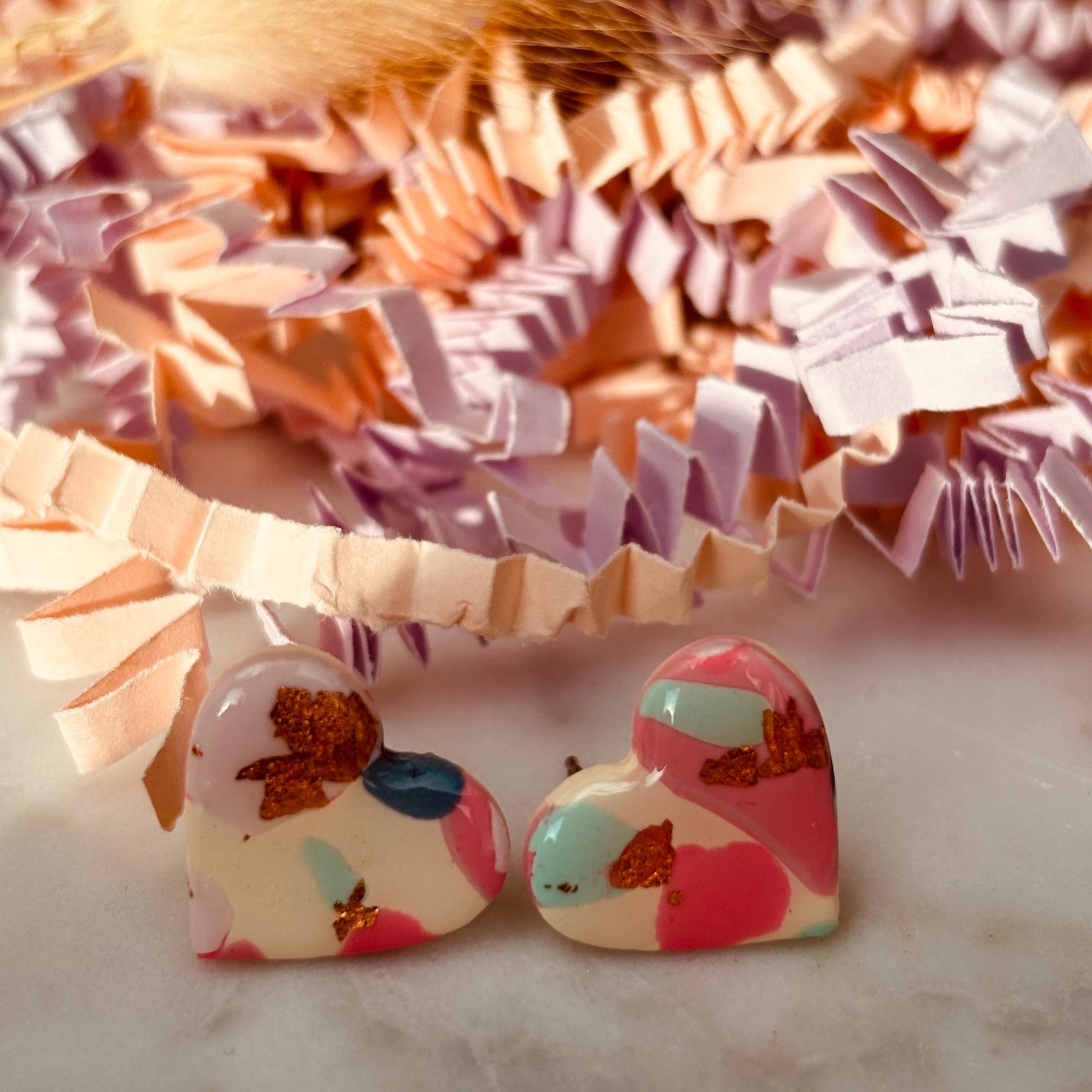Soft pink heart-shaped stud earrings with rose gold accents, handmade with polymer clay.