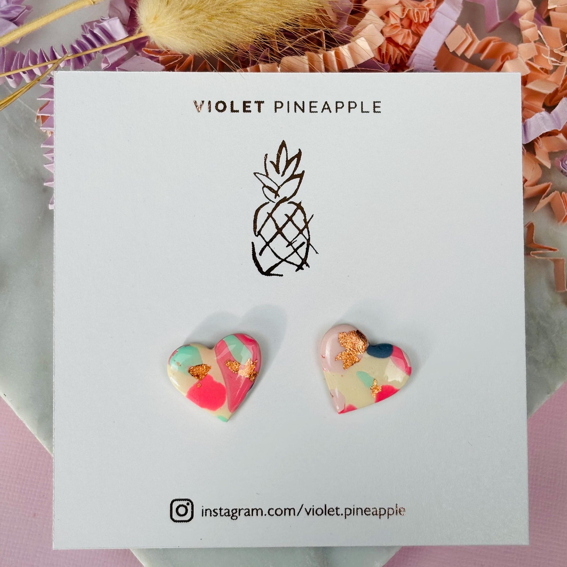 Soft pink heart-shaped stud earrings with rose gold accents, handmade with polymer clay.