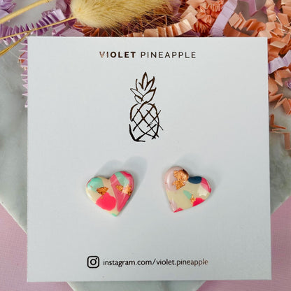 Soft pink heart-shaped stud earrings with rose gold accents, handmade with polymer clay.