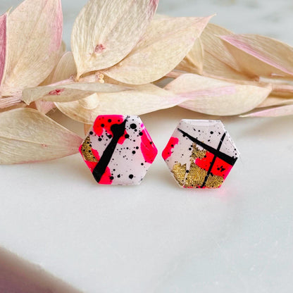 Bold abstract hexagon stud earring featuring white, neon pink, gold foil, and black ink splatter, handmade from polymer clay.