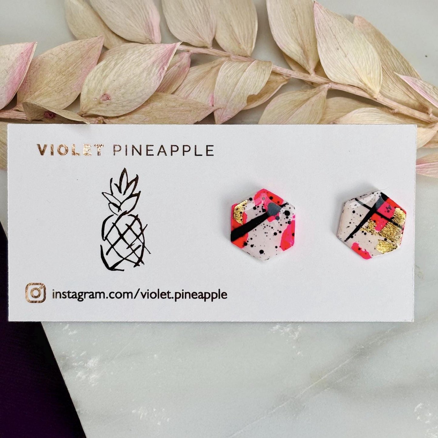 Bold abstract hexagon stud earring featuring white, neon pink, gold foil, and black ink splatter, handmade from polymer clay.