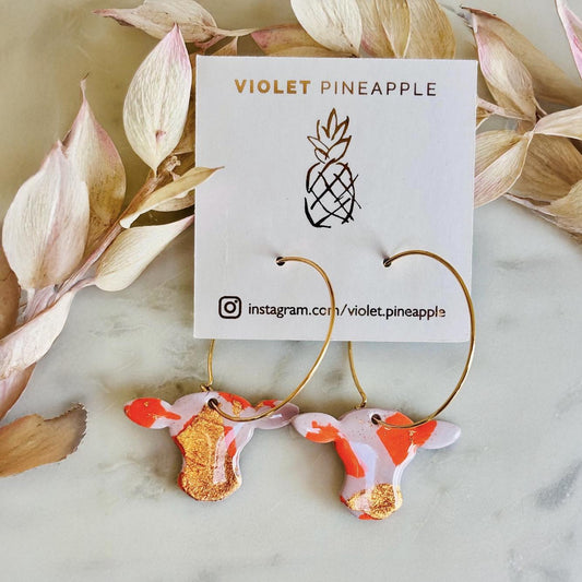 Close-up of vibrant orange cow hoop earring with rose gold foil detail.