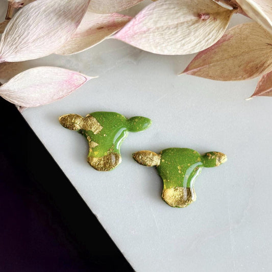 Close-up of small green cow stud earrings with gold foil.