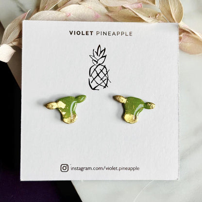 Close-up of small green cow stud earrings with gold foil.