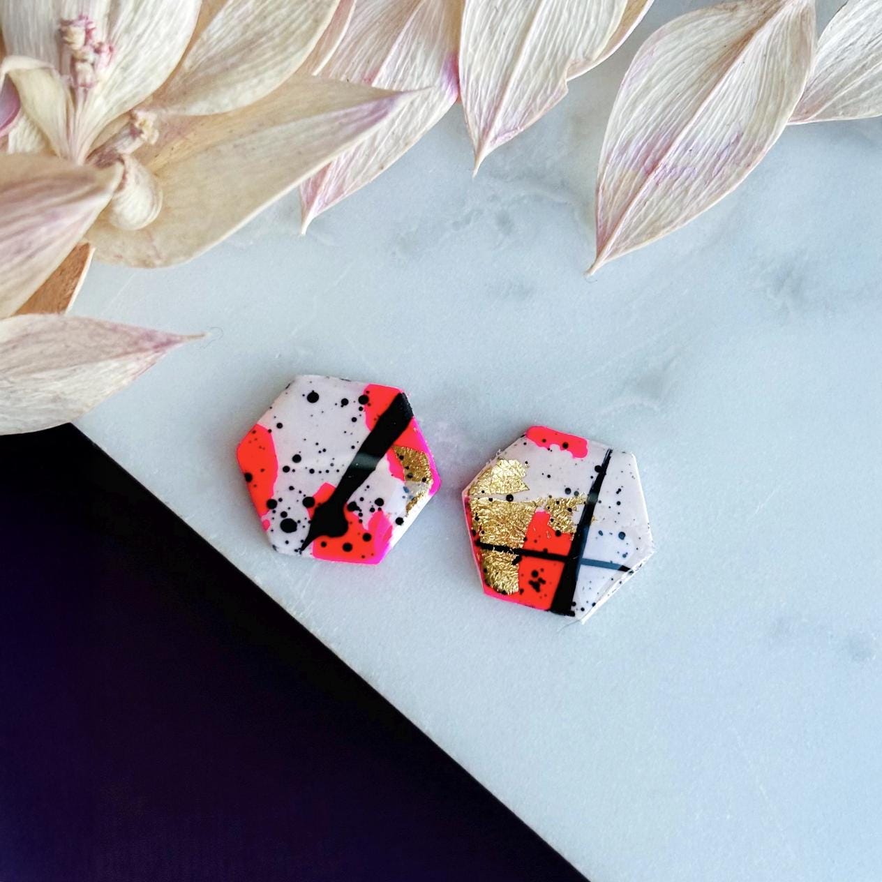 Bold abstract hexagon stud earring featuring white, neon pink, gold foil, and black ink splatter, handmade from polymer clay.