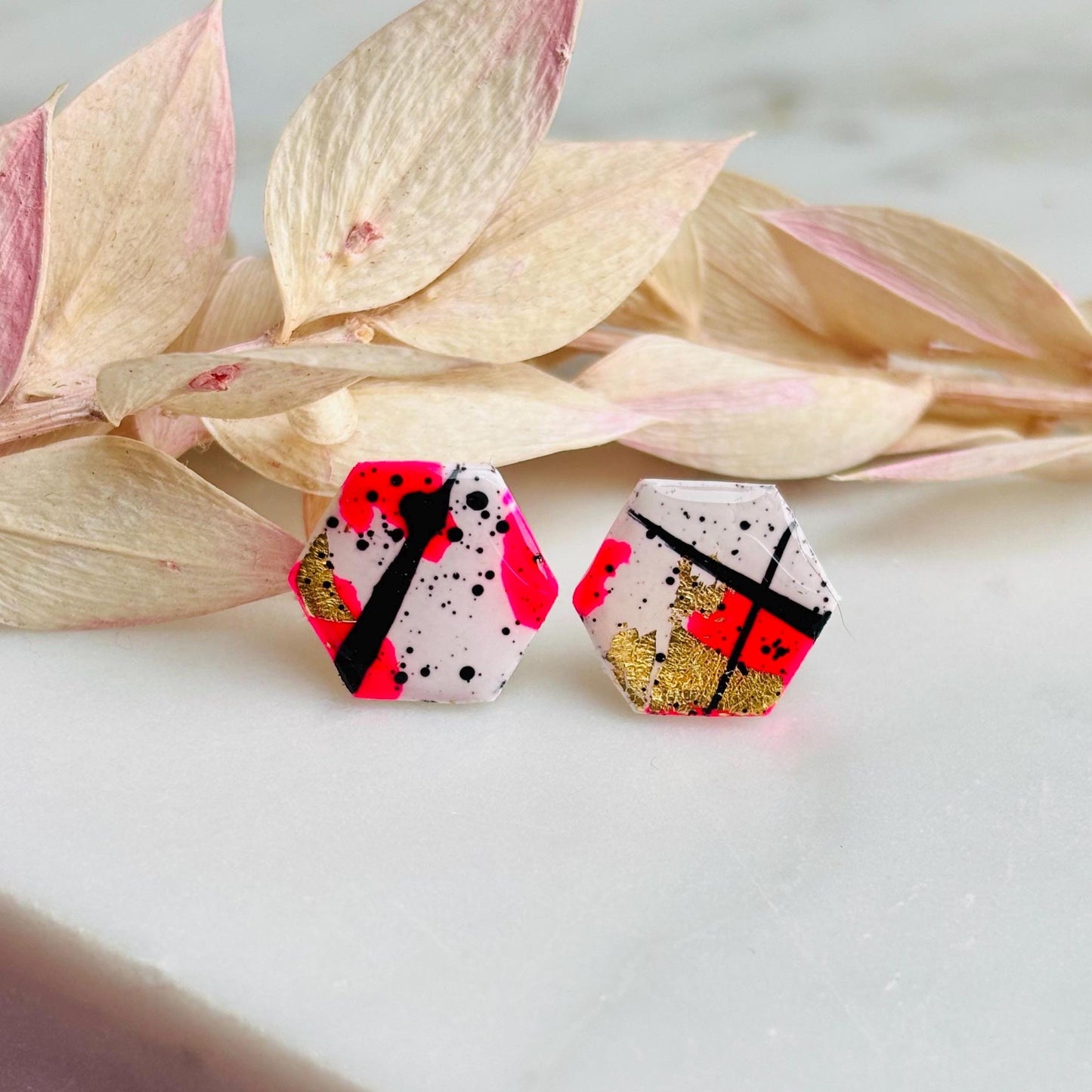 Bold abstract hexagon stud earring featuring white, neon pink, gold foil, and black ink splatter, handmade from polymer clay.