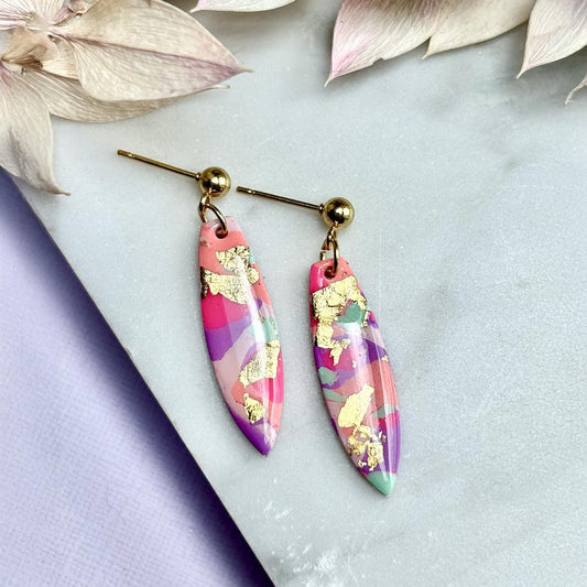 Colourful surfboard-shaped surf earrings with gold foil details, handmade from polymer clay, featuring hypoallergenic surgical stainless steel posts and backings.