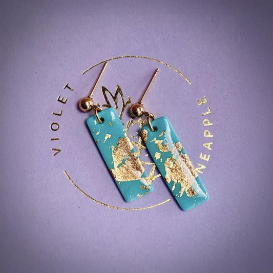 Teal earrings with gold accents on a purple background