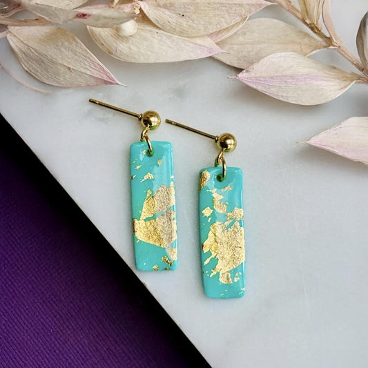 Bold, handmade teal polymer clay drop earrings with elegant gold foil detailing, shown from a close-up angle.