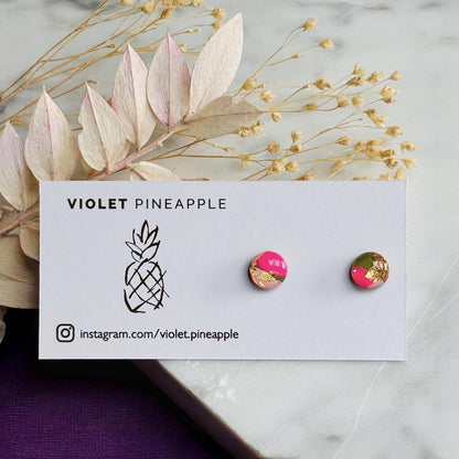 Pair of earrings on a 'Violet Pineapple' branded card with decorative leaves in the background.
