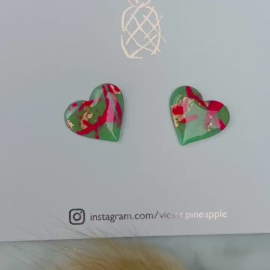 Vibrant neon pink heart-shaped stud earrings, handmade with polymer clay. Features an abstract design with gold foil accents.