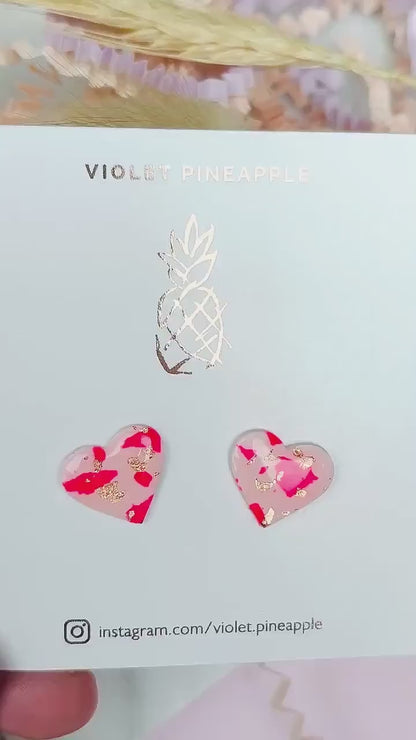 Vibrant pink heart-shaped stud earrings, handmade with polymer clay. Features rose gold leaf accents