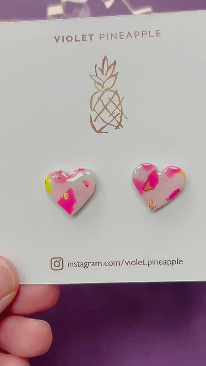 Delicate pastel-coloured heart-shaped stud earrings, handmade with polymer clay. Features soft pink, and yellow with gold leaf accents.