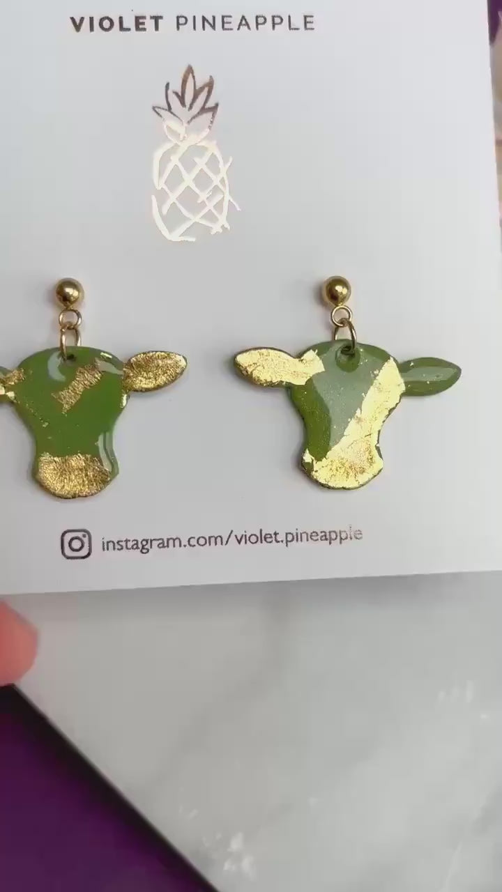 Cute cow drop stud earrings with olive green and gold foil details, handmade with polymer clay.