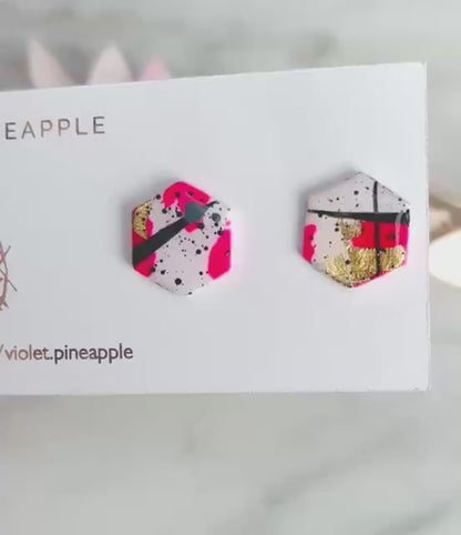 Bold abstract hexagon stud earring featuring white, neon pink, gold foil, and black ink splatter, handmade from polymer clay.