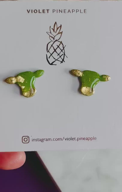 Close-up of small green cow stud earrings with gold foil.